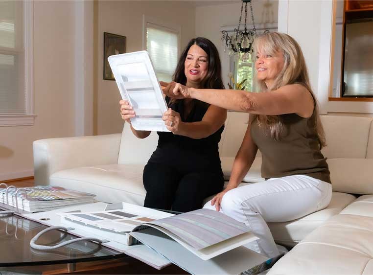 Two women sitting on a couch looking at a book of fabric samples